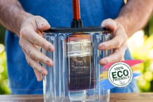 A person holding a clear eco-friendly BruKon paint brush cleaner container with one brush inside